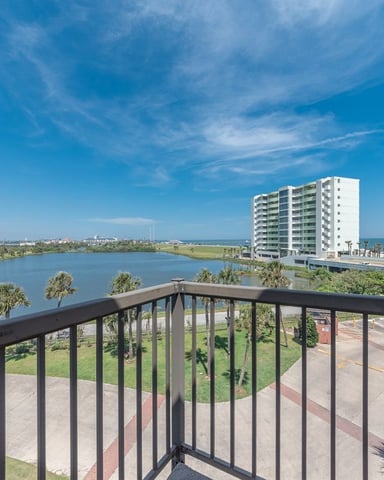 Balcony view of coastal bay with white high-rise building, palm trees, and Gulf of Mexico shoreline under blue sky