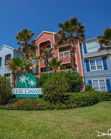 Colorful beachfront condominiums with palm trees and manicured lawn under clear blue sky
