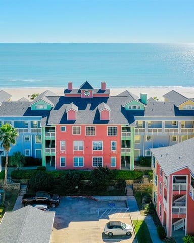 Colorful beachfront resort complex with blue, red, yellow, and green buildings facing sandy beach and turquoise ocean.