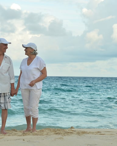 Couple holding hands on sandy beach with ocean and cloudy sky in background