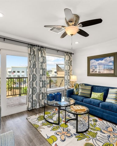 Bright living room with blue sofa, patterned rug, and glass doors opening to balcony with ocean view