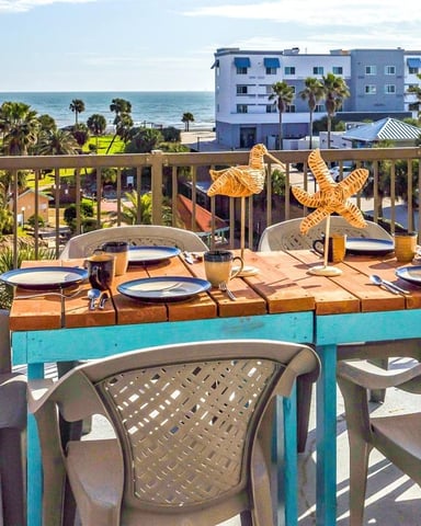 Beachfront balcony dining table set with ocean view, palm trees, and coastal apartment buildings