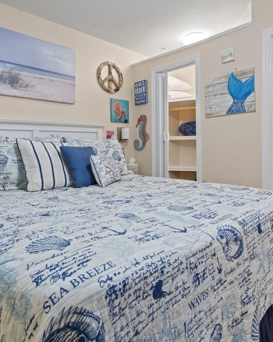 Coastal-themed bedroom with blue and white nautical bedding, beach artwork, and ensuite bathroom with flamingo shower curtain