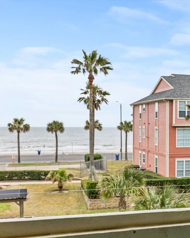 Beachfront view from balcony with palm trees, colorful beach houses, and ocean beyond