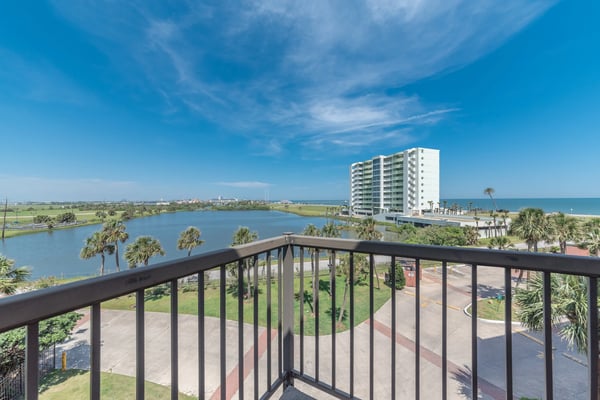 Balcony view of coastal lagoon, high-rise building, palm trees, and ocean under blue sky