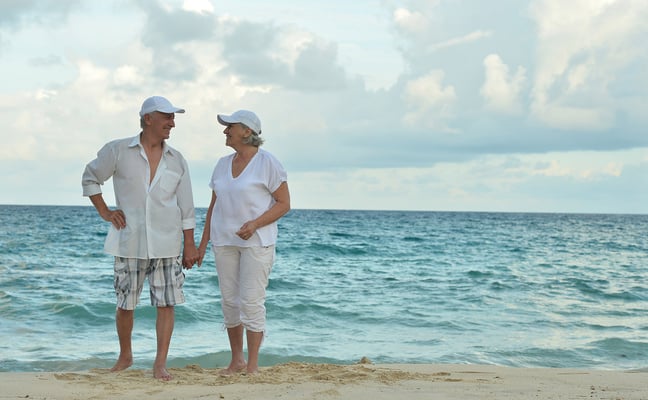 Couple holding hands on sandy beach with ocean and cloudy sky in background